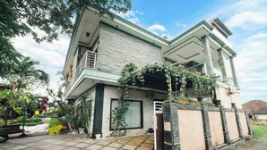 A modern two-story house with a stone facade, a balcony, and a gated entrance. - Aeena Homestay (Ungasan)