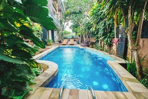 A rectangular swimming pool with a tiled edge, surrounded by lush greenery and a few lounge chairs. - Aeena Homestay (Ungasan)