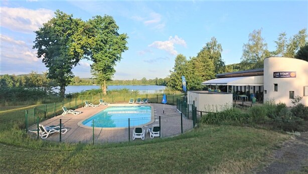 A swimming pool with lounge chairs, a restaurant named "LE TITAN," and a large tree in the background.