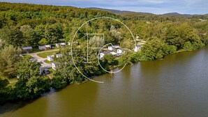 An aerial view of a lakeside property with several cabins and a small house, surrounded by dense forest and hills.