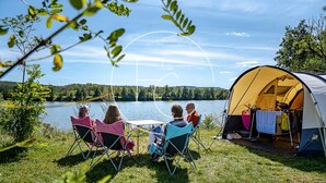 A group of people seated at a table outdoors, with a tent and camping gear nearby.