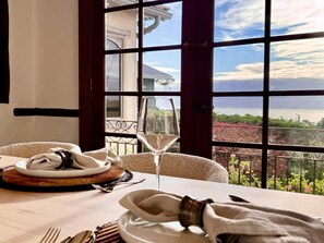 A dining table set with plates, cutlery, and a glass, overlooking a scenic view of the sea and greenery.