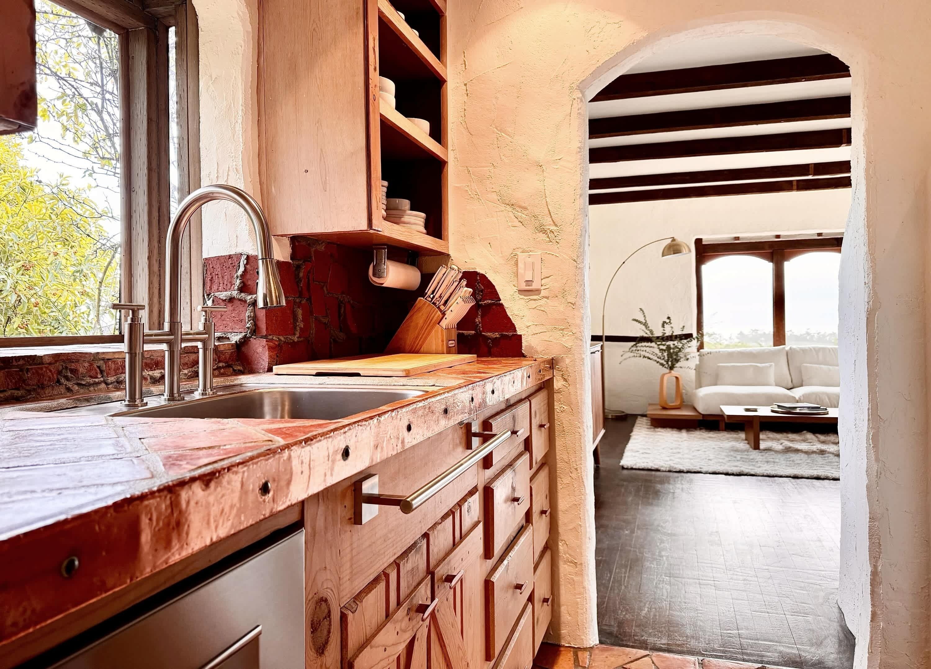 A rustic kitchen with a wooden countertop, a sink, and a wooden cabinet. There is a window with a view of trees outside.