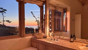 Un baño con una ventana grande, un lavamanos, un espejo y un banco.