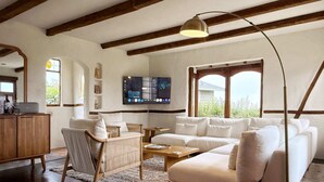 Una sala moderna con un sofá blanco, una mesa de centro de madera, un sillón de mimbre y un televisor montado en la pared.