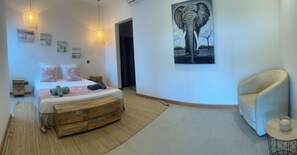 A modern bedroom with a bed, bedside tables, a wooden bench, a chair, and artwork on the walls.