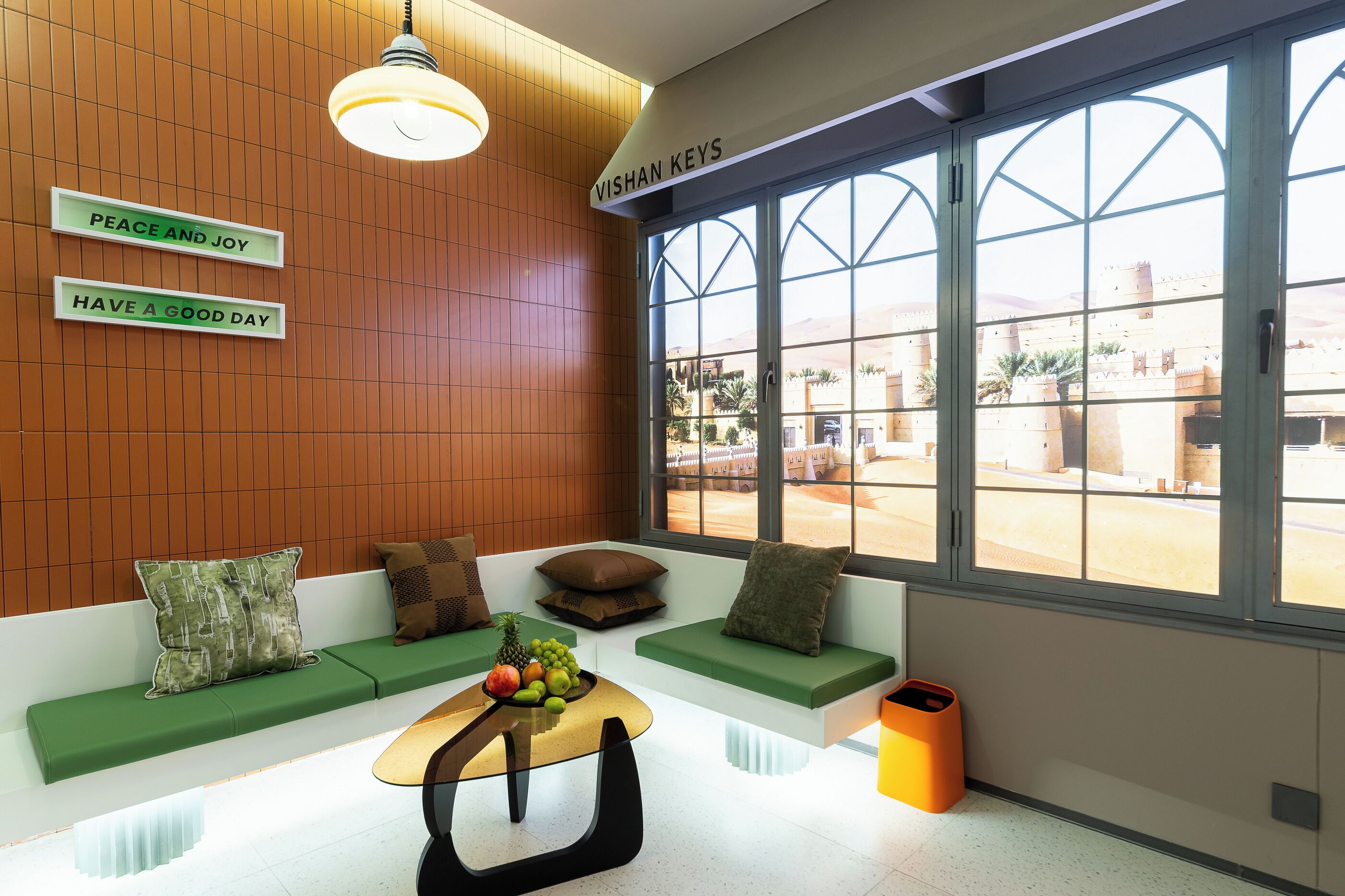 A modern lobby with a wooden wall, green seating, a fruit bowl on a table, and a large window with a view of buildings.