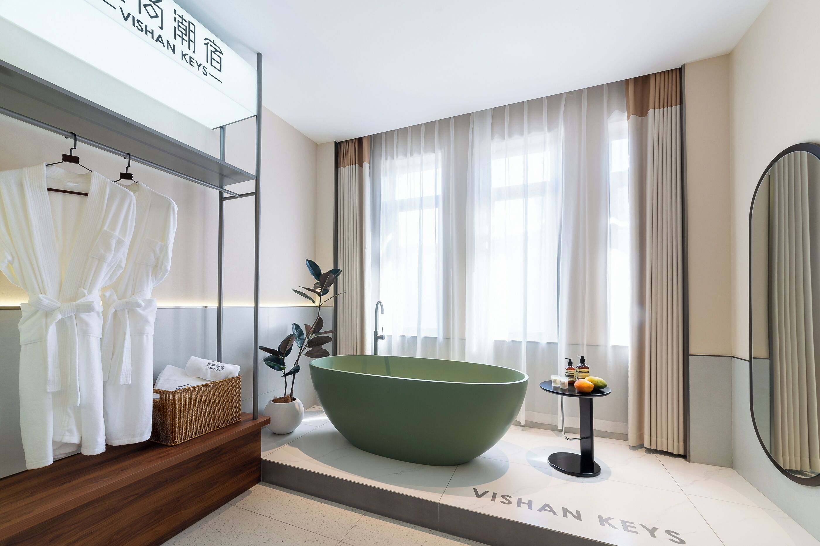 A modern bathroom with a large green bathtub, a wooden vanity, a hanging robe rack, and a large mirror.