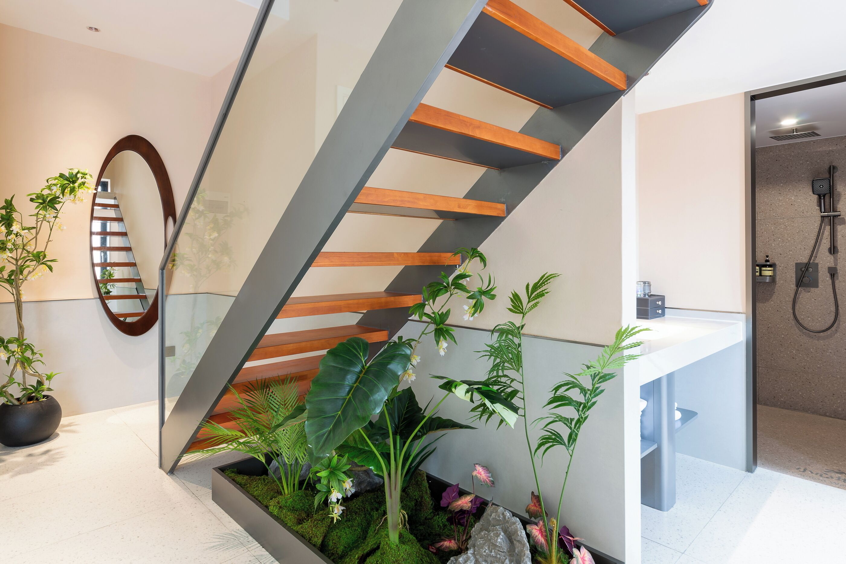 A modern staircase with glass railings and wooden steps, leading to a bathroom with a shower and sink.