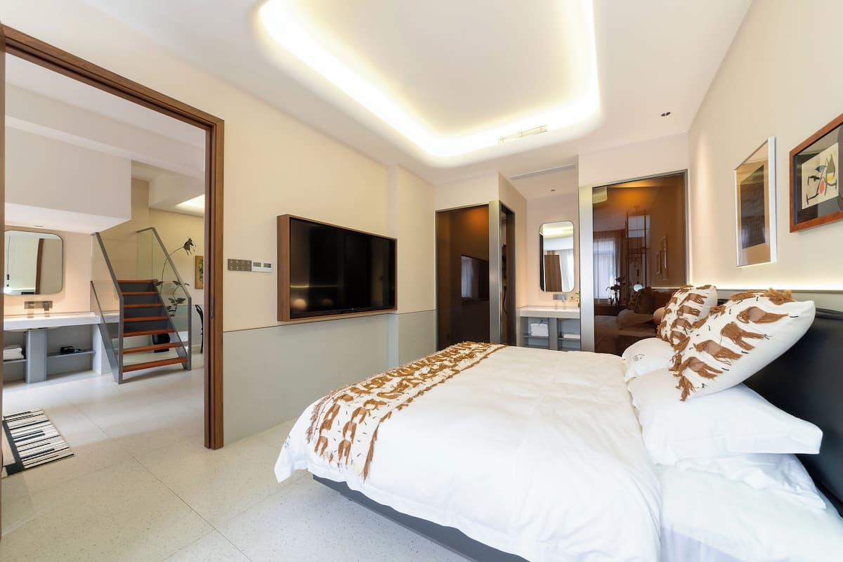 Une chambre d’hôtel moderne dotée d’un grand lit, d’un téléviseur fixé au mur, d’un bureau avec une chaise et d’un escalier menant à un autre niveau.