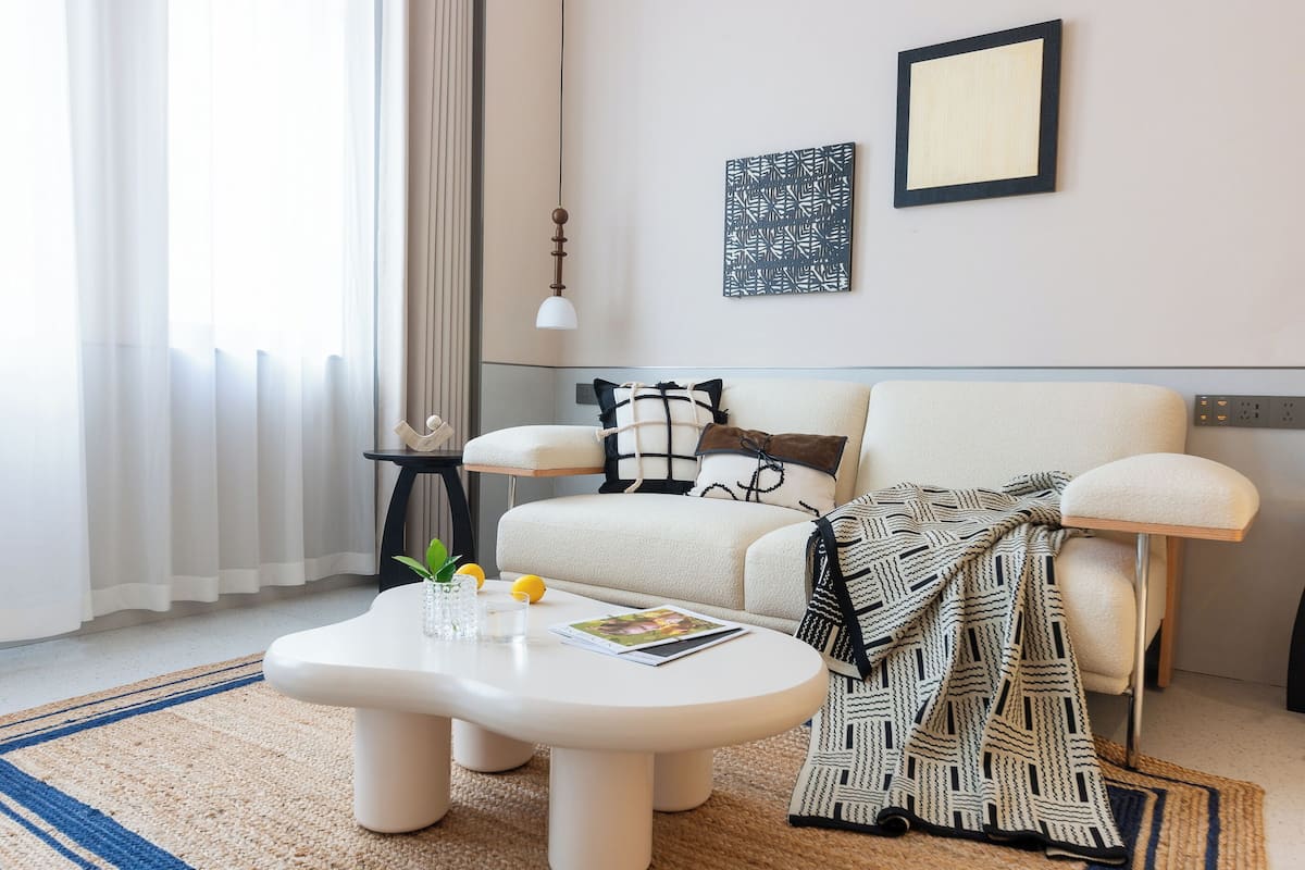 Un salon moderne avec un canapé, une table basse et une lampe. Il y a une fenêtre avec des rideaux et un radiateur.