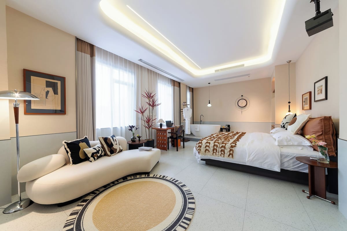 Une chambre d’hôtel moderne avec un canapé incurvé, un grand lit, un bureau et une baignoire.