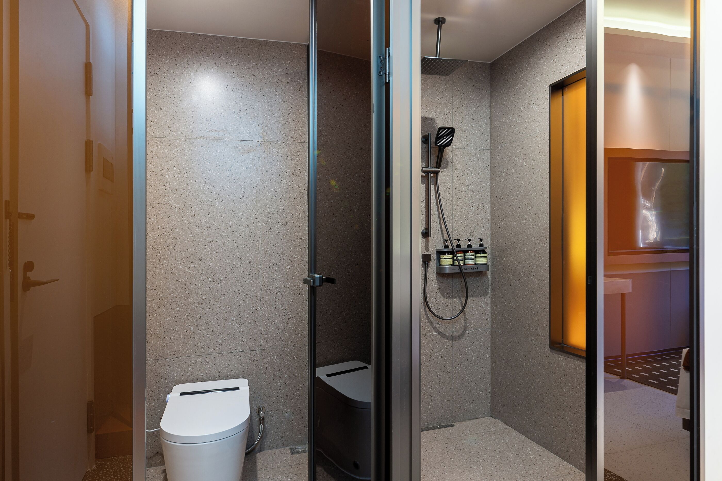 A modern bathroom with a glass shower enclosure, a toilet, and a sink with a soap dispenser.