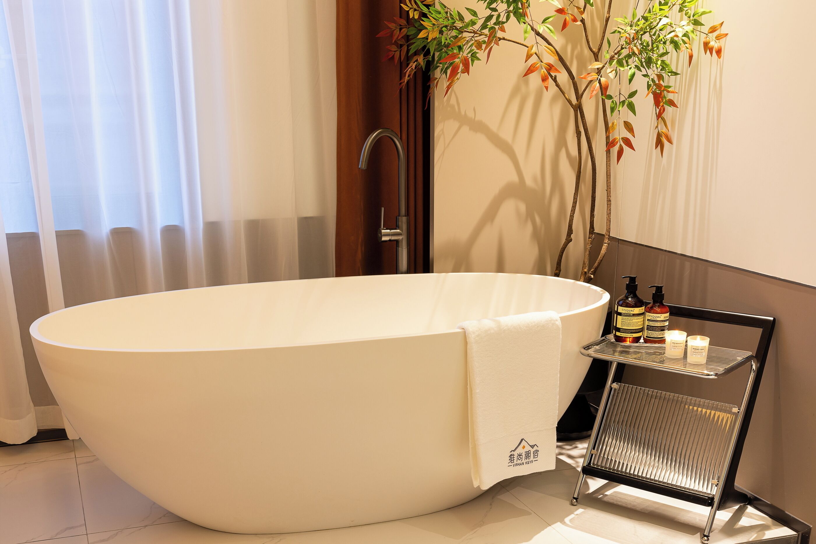 A modern bathroom with a large oval bathtub, a wooden door, a wall-mounted shelf with toiletries, and a potted plant.