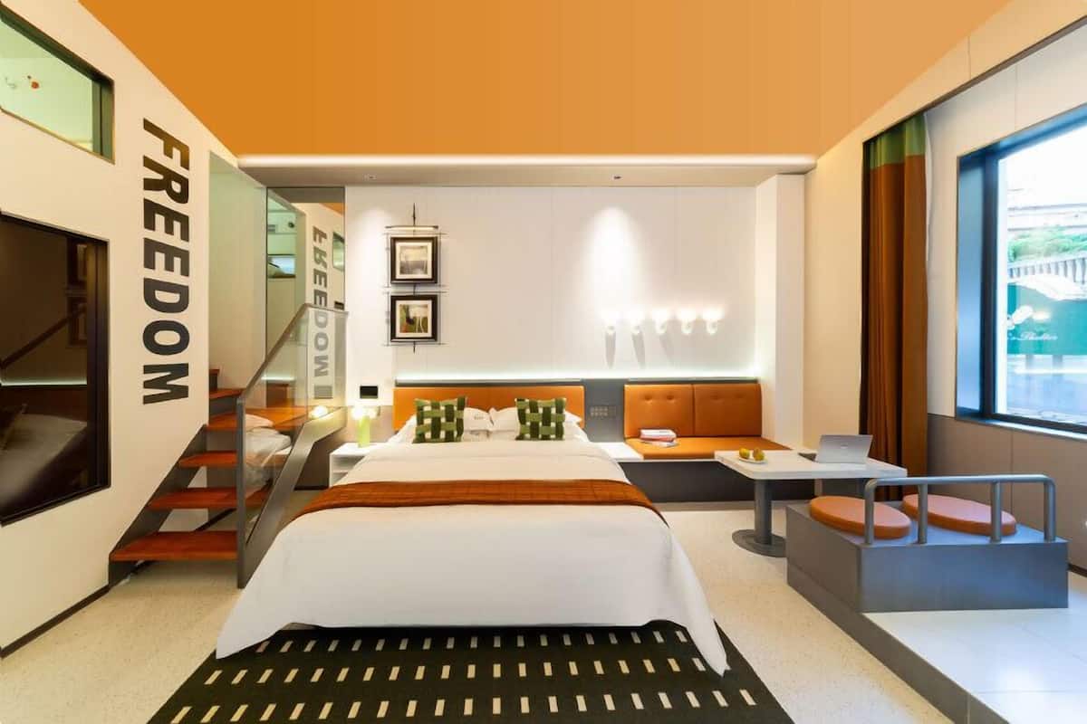 Une chambre d’hôtel moderne, dotée d’un grand lit, d’un bureau, d’un ordinateur portable et offrant une vue sur l’extérieur.