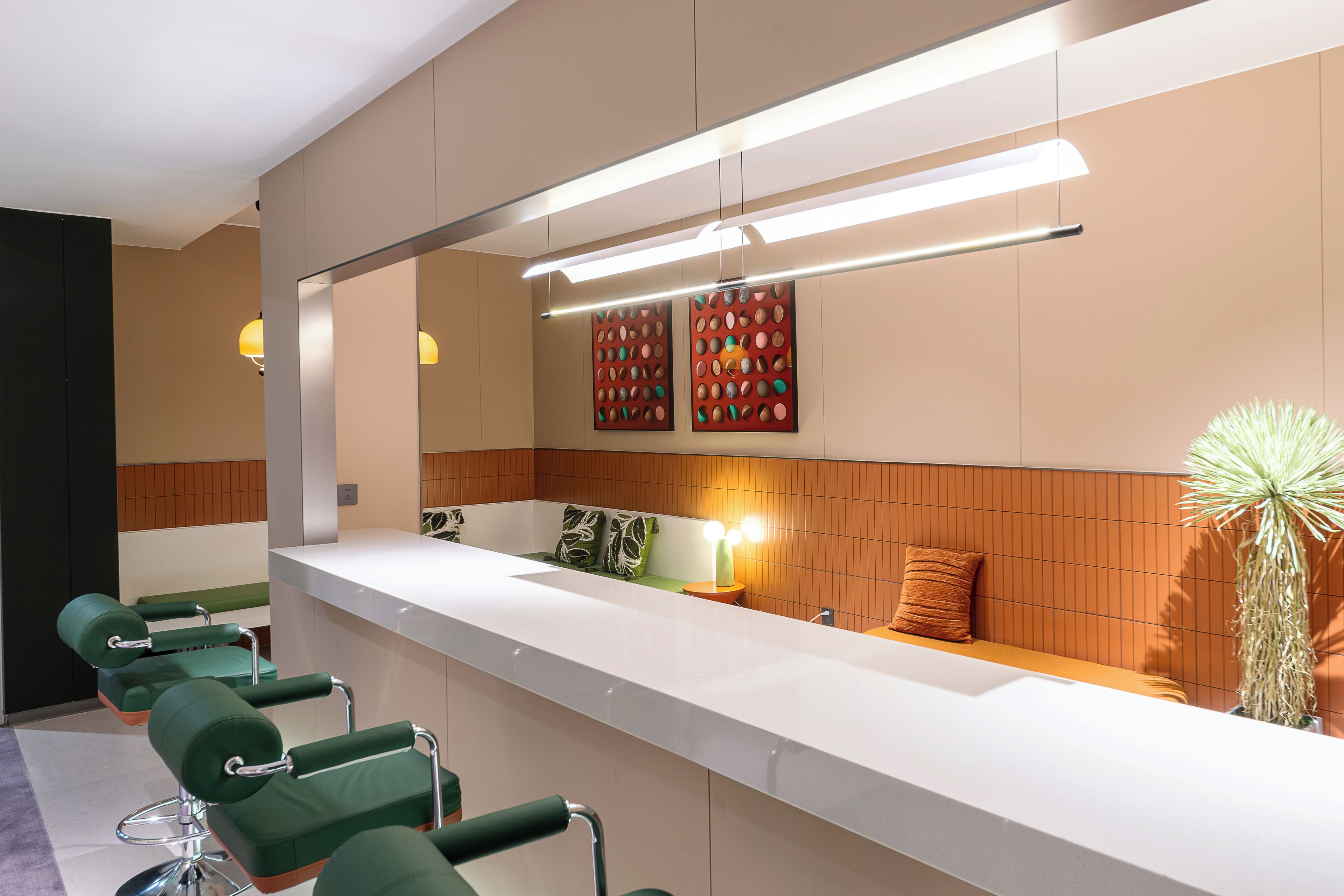 Een moderne receptiebalie met een lange toonbank, groene stoelen, een grote spiegel en een muur met decoratief kunstwerk.