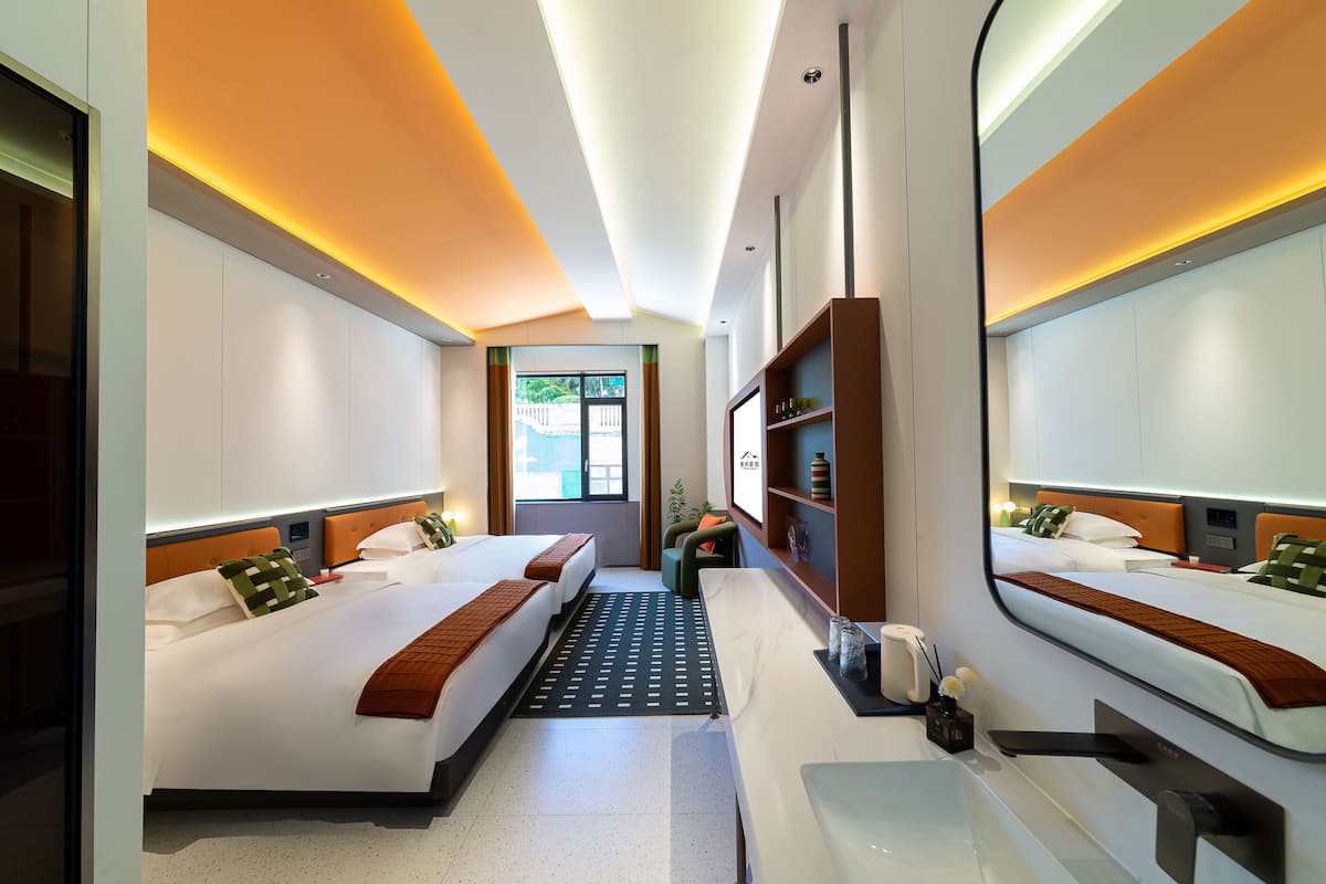 Une chambre d’hôtel moderne avec deux lits, un grand miroir, un bureau et une vue sur l’extérieur.