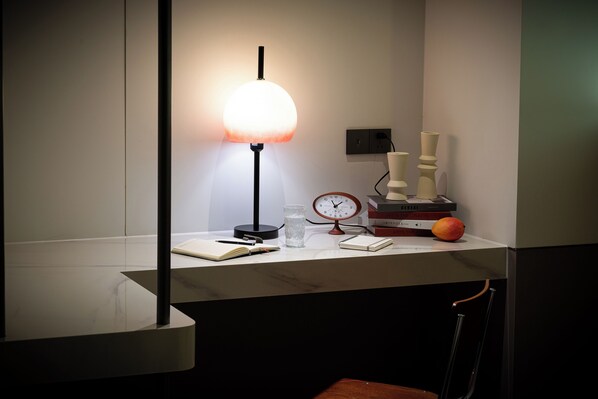 Un bureau avec une lampe, une horloge, des livres et un fruit.