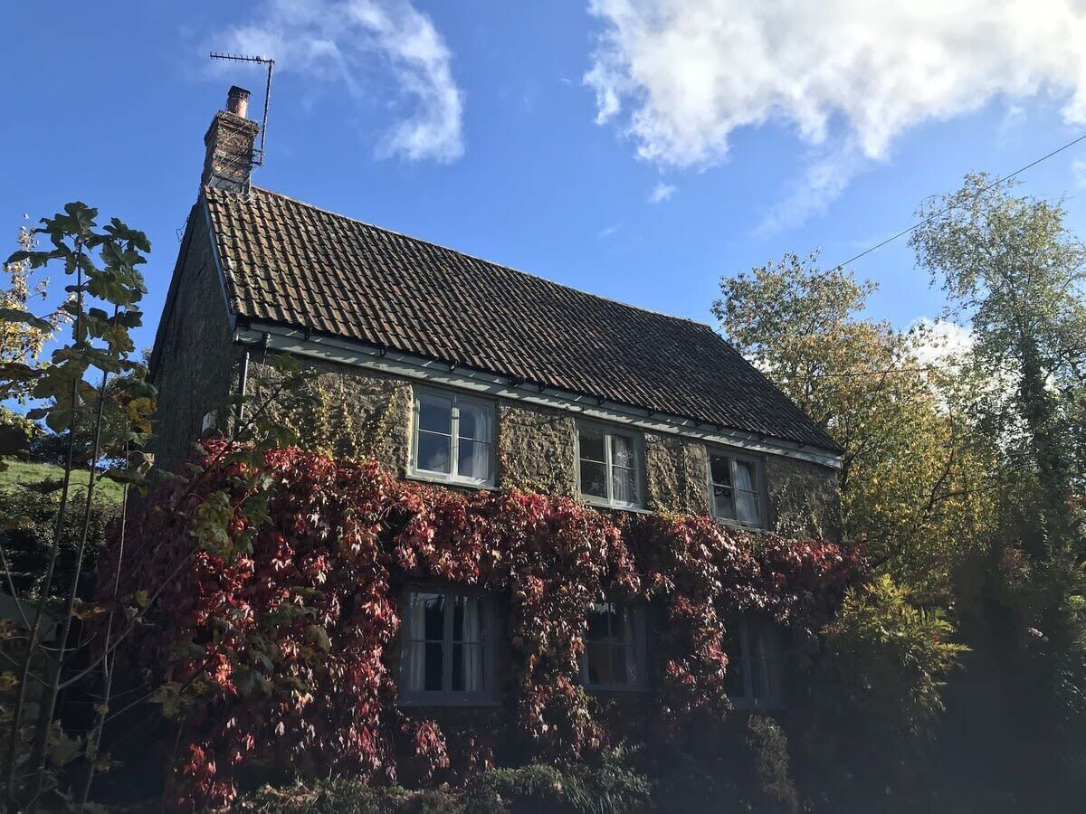 Une maison en pierre avec un toit de tuiles, des murs recouverts de lierre et une cheminée.