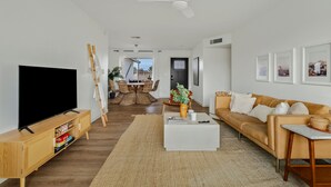 Un salon moderne doté d’un téléviseur à écran plat, d’une table basse blanche, d’un canapé et d’un coin repas avec des meubles en osier.