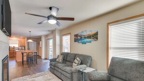 A living room with a grey sofa, a coffee table, and a ceiling fan. There is a kitchen in the background with wooden cabinets and a dining area. - 4 Mi to Granby Ranch: Cabin w/ Hot Tub Access! (Granby)