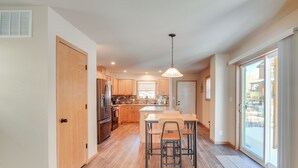 A modern kitchen with wooden cabinets, a central island, and a dining area with metal chairs. - 4 Mi to Granby Ranch: Cabin w/ Hot Tub Access! (Granby)
