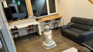 A modern living room with a black leather sofa, a wooden coffee table, a white table, and a unique decorative heater. - Train Line Field (Tobetsu)
