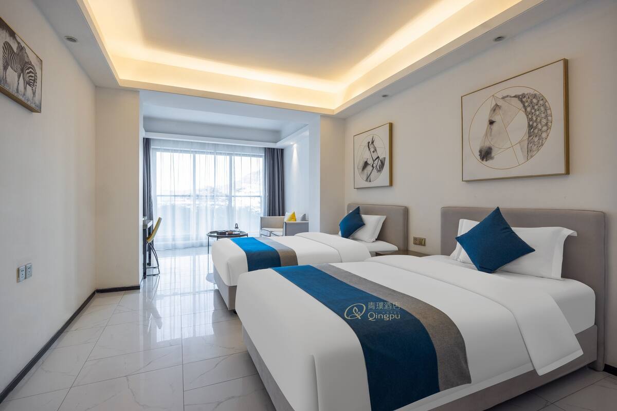 A hotel room with two beds, a large window, and artwork on the walls.