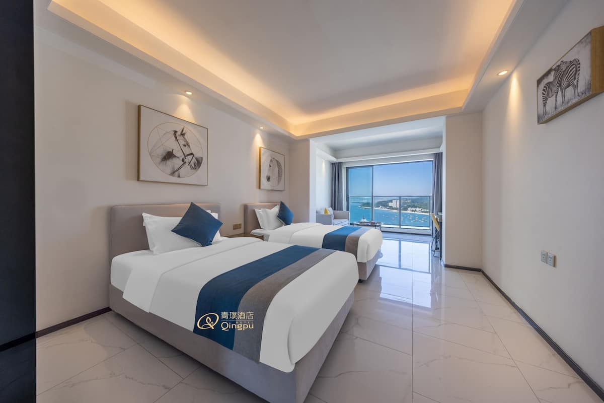 A modern hotel room with two beds, a large window, and artwork on the walls.