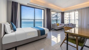 Una habitación de hotel moderna con una cama grande, un sofá, una mesa de comedor y vistas al océano.