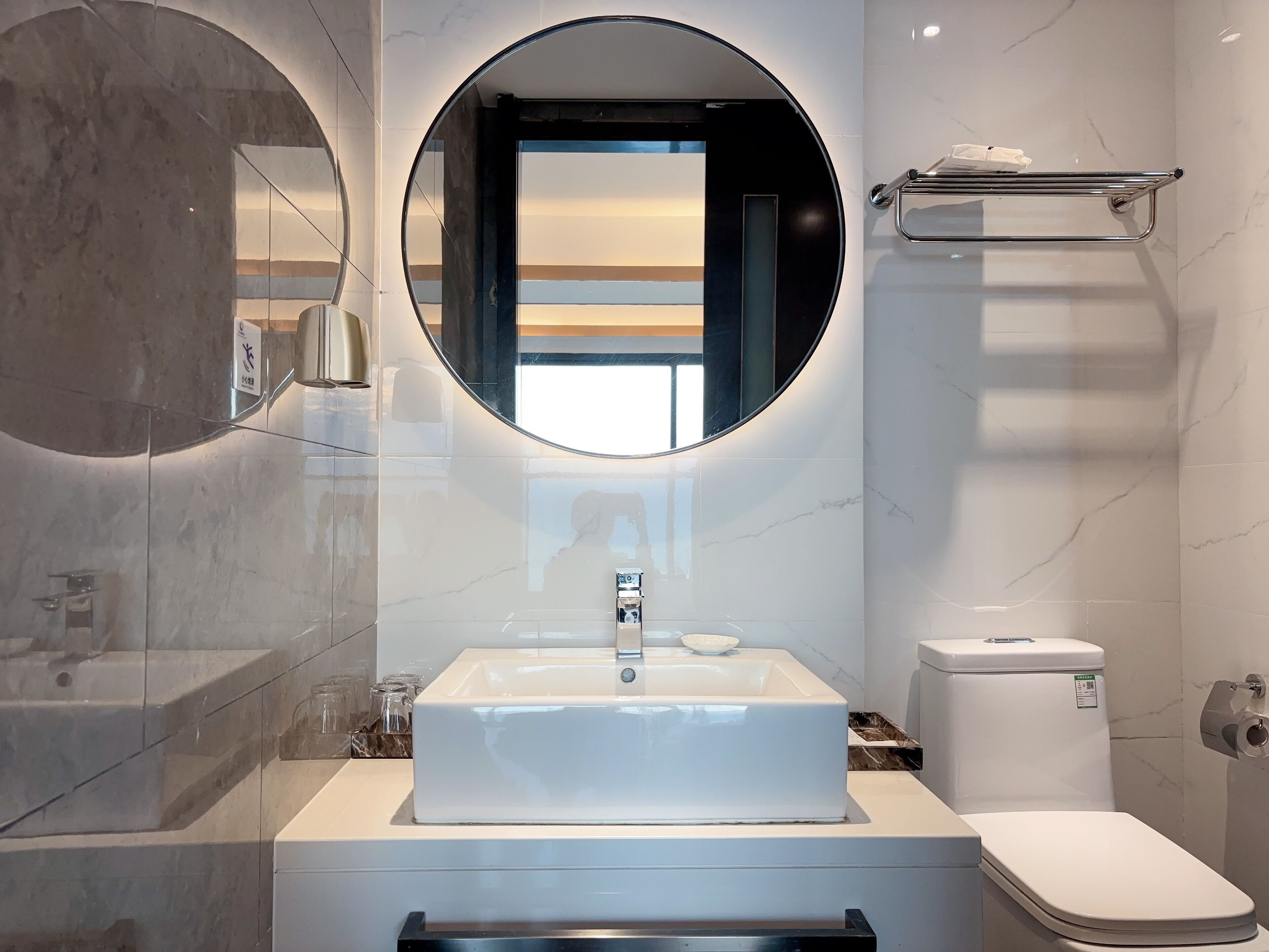 A modern bathroom with a large oval mirror, a rectangular sink, and a toilet.