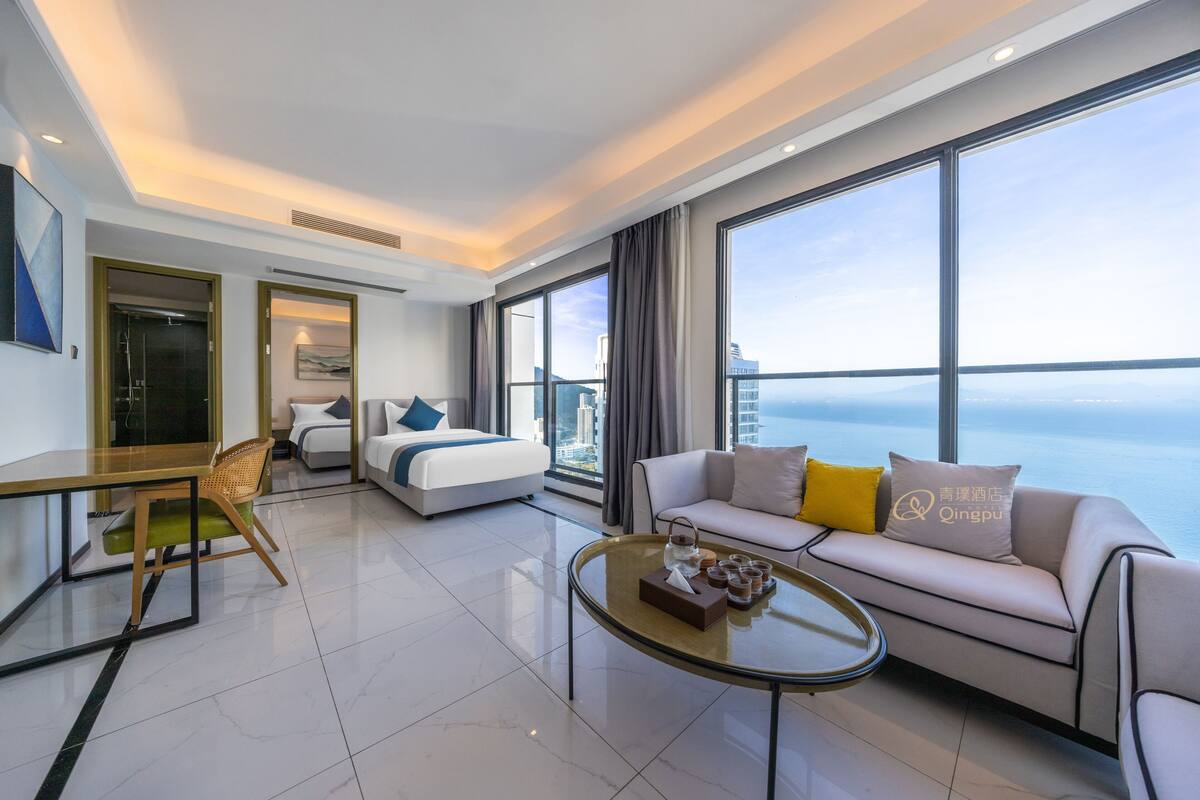 A modern hotel room with a bed, sofa, and dining area.