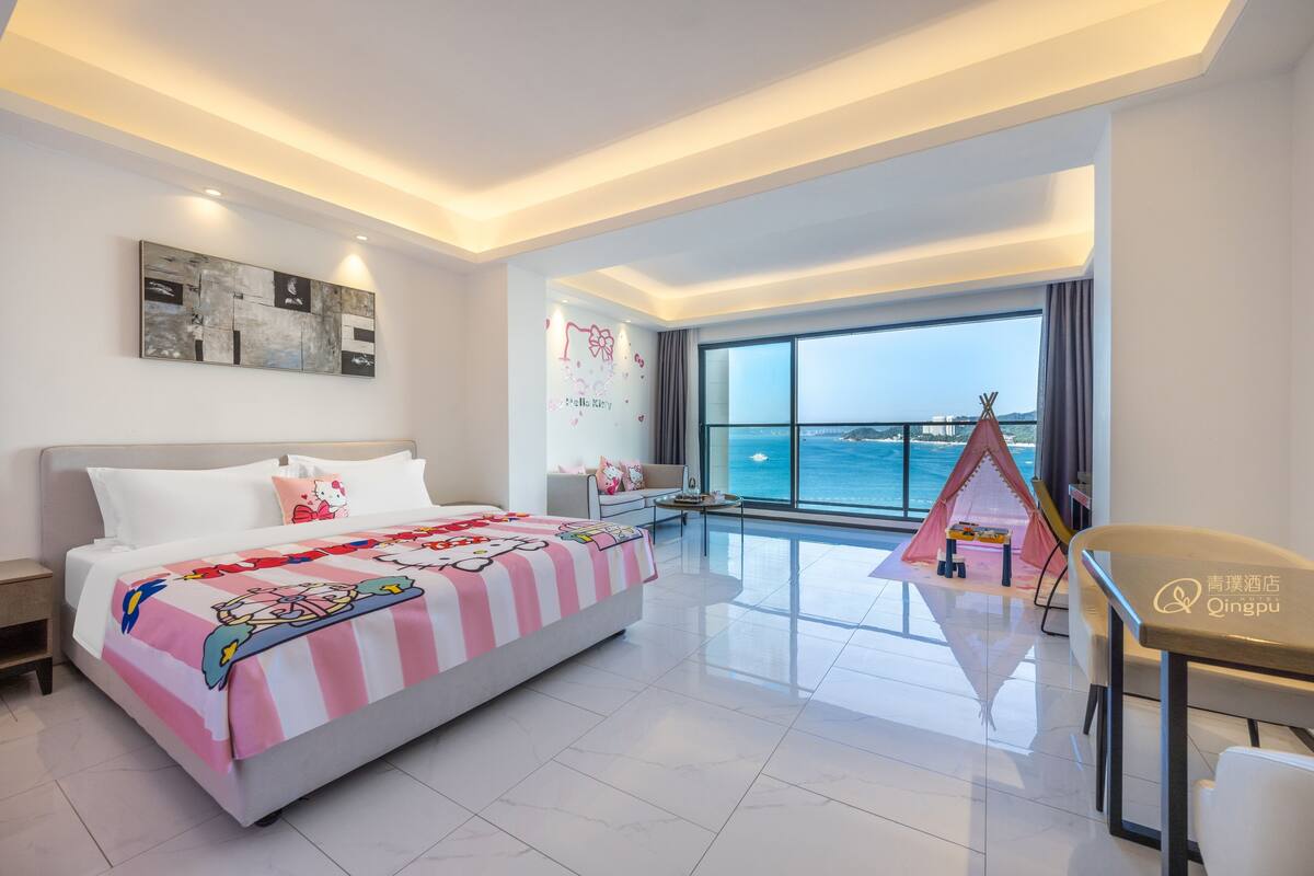 A modern hotel room with a large bed, a desk, and a view of the sea.