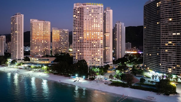 Un paisaje urbano costero al anochecer con rascacielos, una playa y un puerto deportivo.