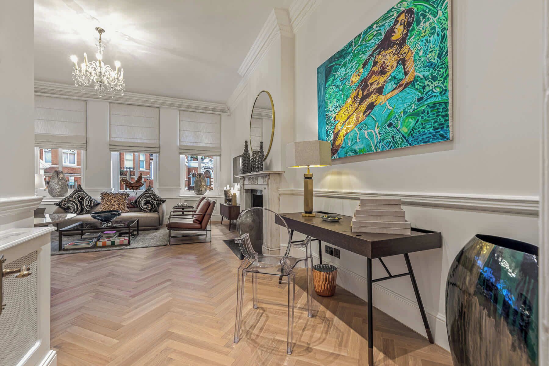 Un salon spacieux agrémenté d’un grand tableau, d’un lustre et d’une cheminée.