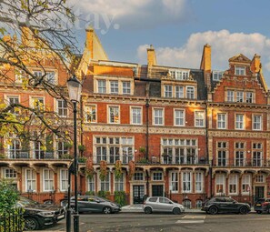 A row of red brick townhouses with multiple windows, a street lamp, and parked cars.