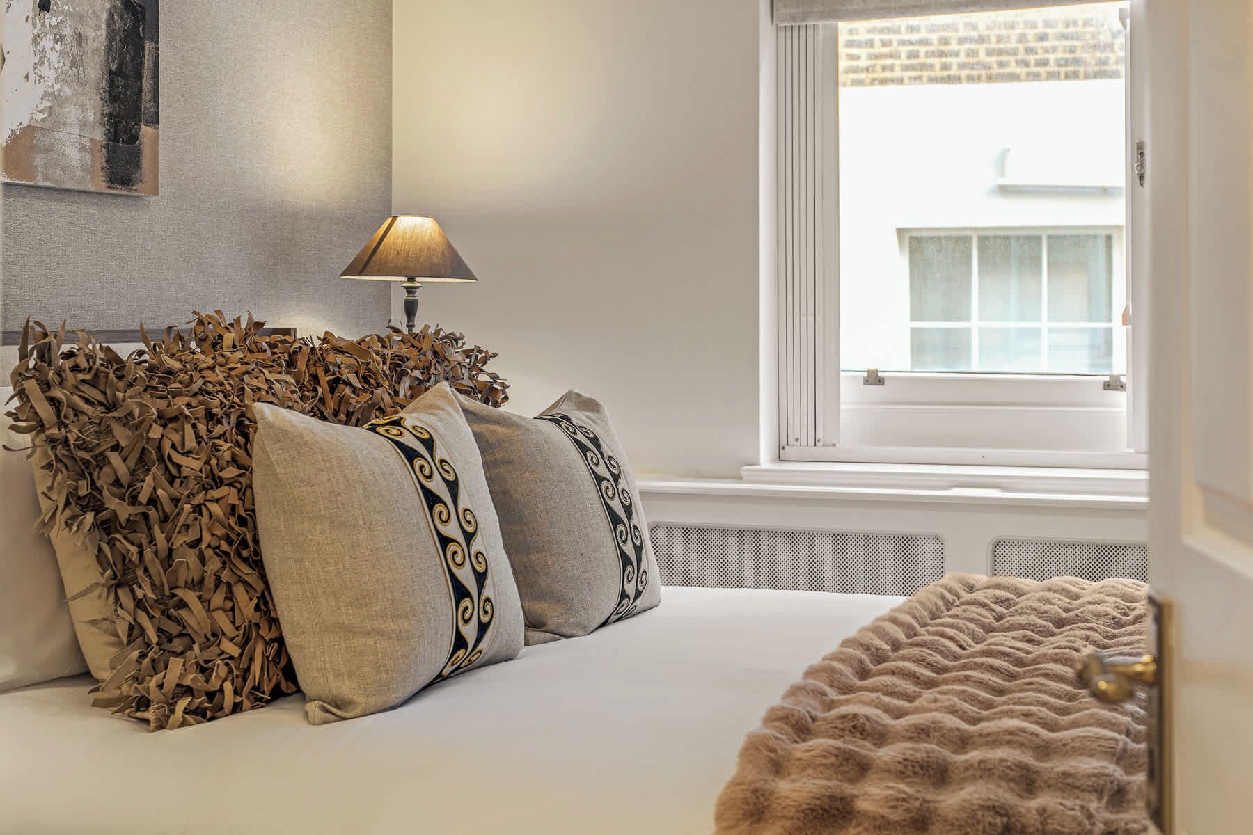 A bedroom with a bed, pillows, a lamp, and a window.
