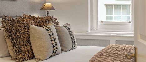 A bedroom with a bed, pillows, a lamp, and a window.