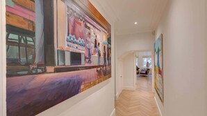 A hallway with a large abstract painting on the left and a smaller one on the right. The hallway has a wooden floor and white walls. - The Gallery - Exquisite Apartment, Kensington (Kensington)