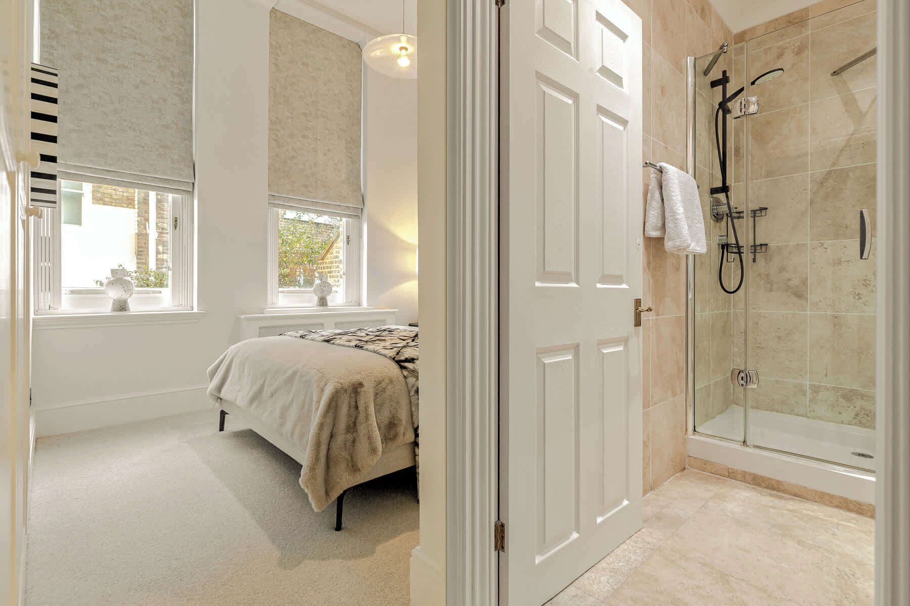 Un dormitorio con una cama, ventana y puerta que da a un baño con ducha.