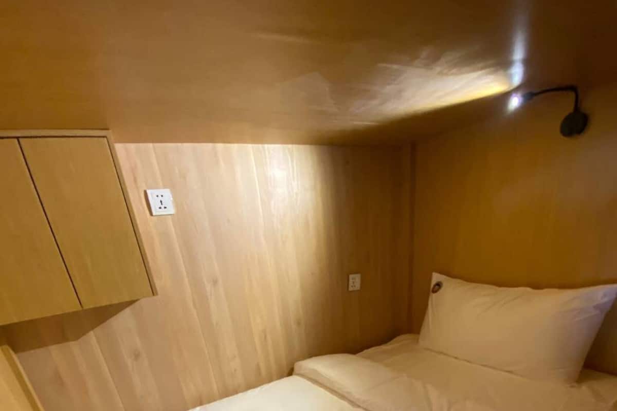 A compact room with a single bed, a small cabinet, and a wall-mounted light fixture.