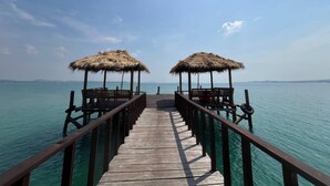 Un muelle de madera que lleva a una playa con sombrillas de paja.