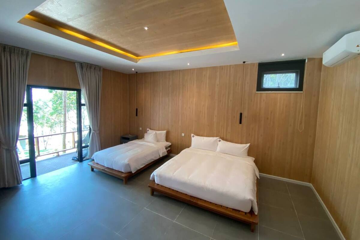 A modern hotel room with two beds, wooden walls, a large window, and a ceiling light fixture.