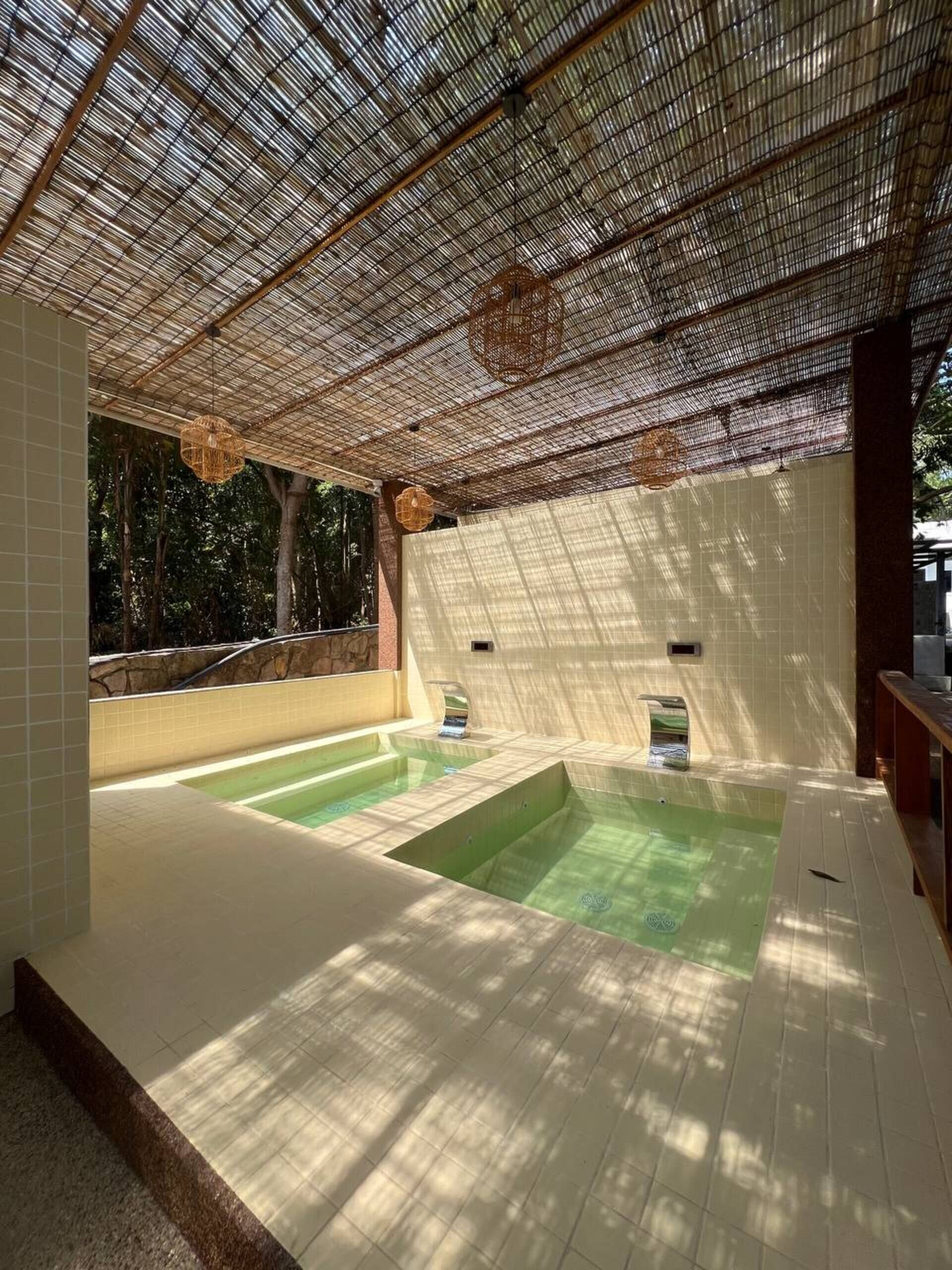 A spa area with two hot tubs under a bamboo roof, surrounded by white tiles and a stone wall.