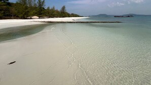 Una playa con aguas cristalinas y poco profundas, una orilla de arena y un muelle a lo lejos.