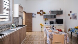A compact kitchen with a dining area, featuring a tiled floor, wooden cabinets, a built-in oven, and a dining table set with plates and a vase of flowers.
