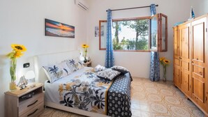 A bedroom with a bed, a nightstand, a wardrobe, a window with curtains, and a painting on the wall.