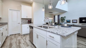 A modern kitchen with granite countertops, white cabinetry, and pendant lighting. - Chic Home, Themed Bedrooms, Game Room, Best Spot (Kissimmee)