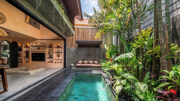 A modern indoor pool area with a clear pool, surrounded by lush greenery and a bamboo wall. - The Mystik Loft Harmony (Canggu)