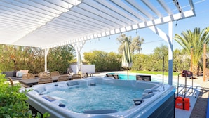 Un bain à remous sous une pergola blanche, avec une piscine et du mobilier d’extérieur.